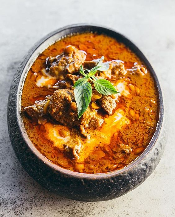 A bowl of rich Khmer red curry featuring tender meat, coconut milk, and spices, garnished with fresh herbs.