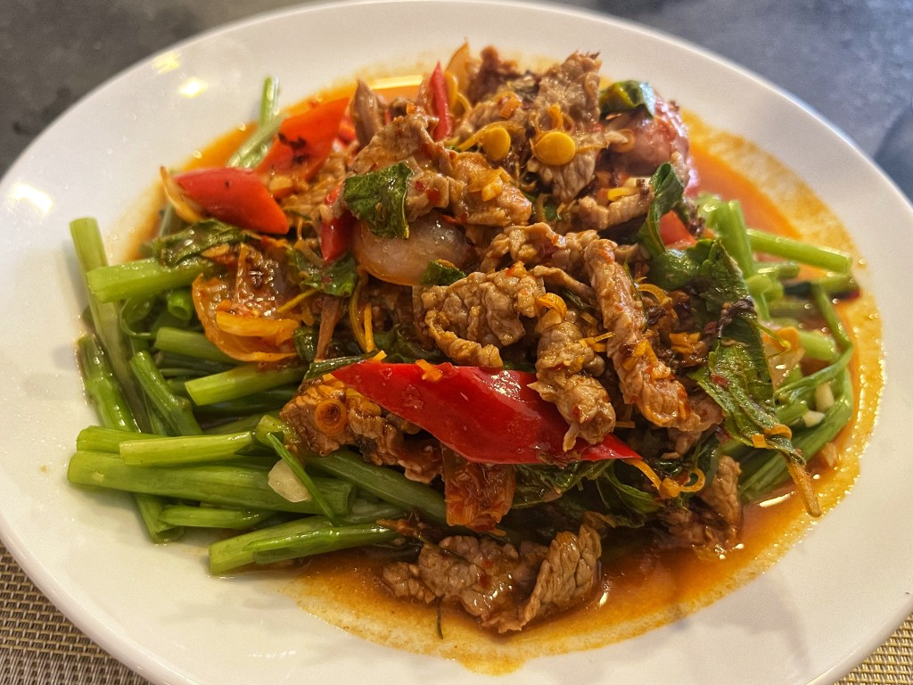 A plate of stir-fried Cambodian beef with vibrant red chilies, green vegetables, and aromatic herbs, drizzled with a savory sauce.