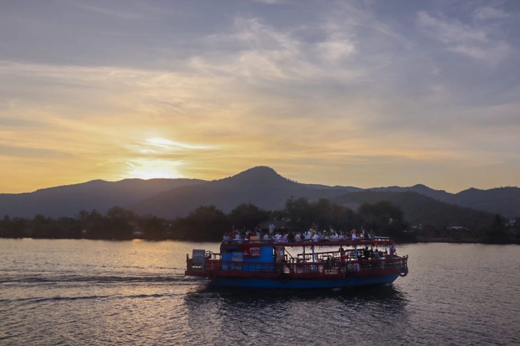 A colorful boat during sunset on a river with silhouettes of mountains in the background.