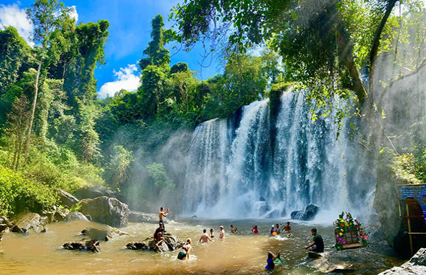 A picturesque waterfall surrounded by lush greenery, with people enjoying the water and rocks in the foreground.