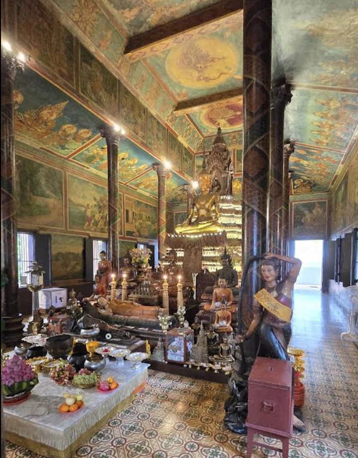 Interior view of the main shrine at Wat Phnom, featuring ornate decorations, a large seated Buddha, and offerings on display.