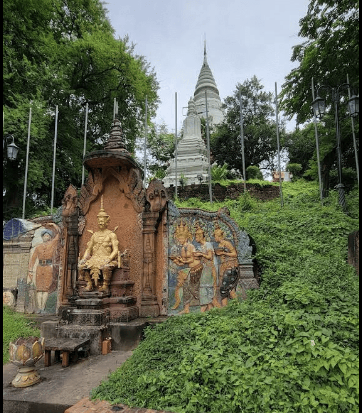 A view of Wat Phnom, the iconic hilltop temple in Phnom Penh, featuring a golden statue seated on a pedestal, surrounded by lush greenery and intricate murals depicting historical figures.