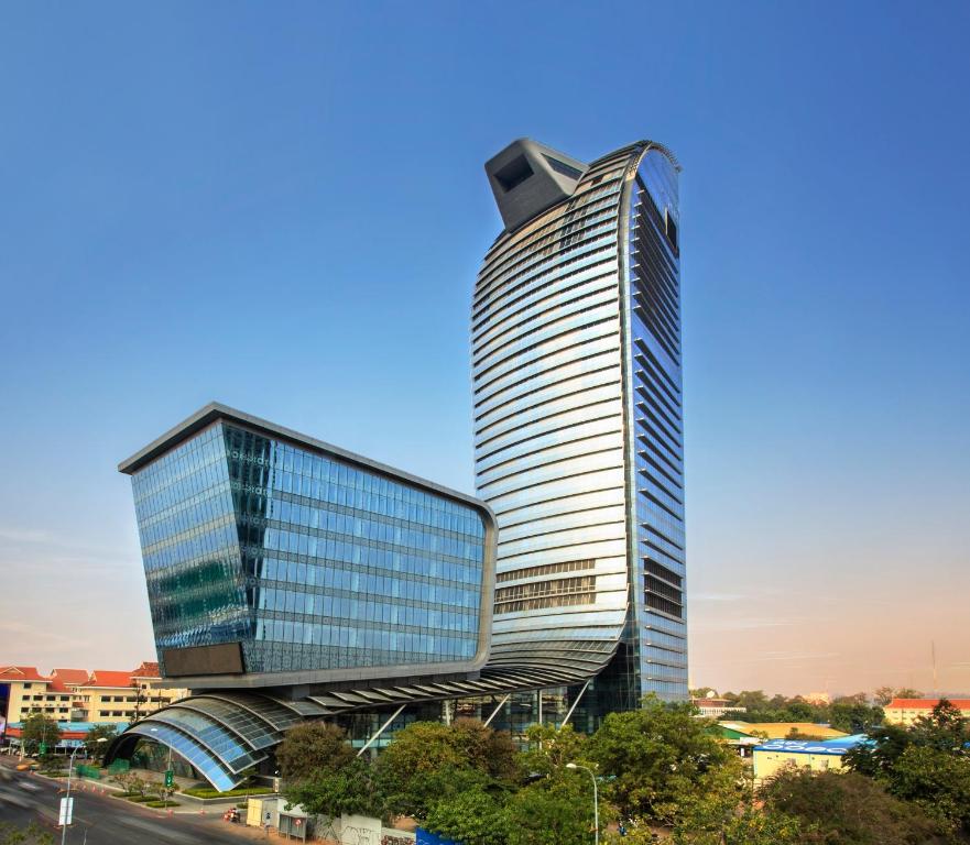 A modern skyscraper with a unique architectural design, featuring a glass façade and an asymmetric structure against a clear blue sky in Phnom Penh, Cambodia.