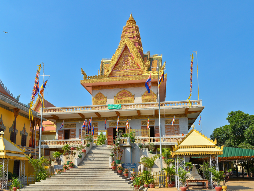 Golden-topped pagoda in Phnom Penh, Cambodia, featuring ornate architecture and colorful flags against a clear blue sky.