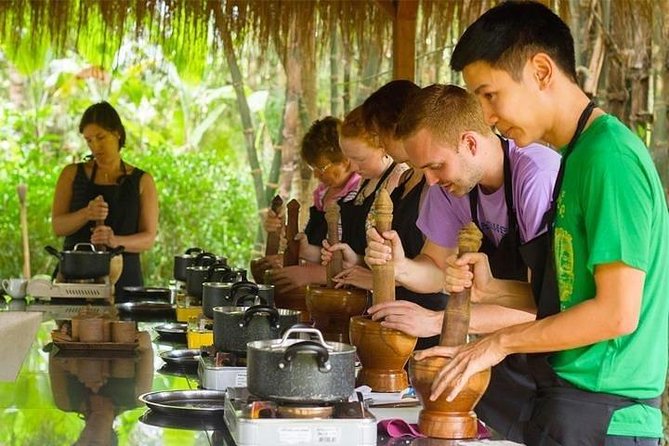 Participants in a cooking class using traditional mortar and pestle at an outdoor setting.