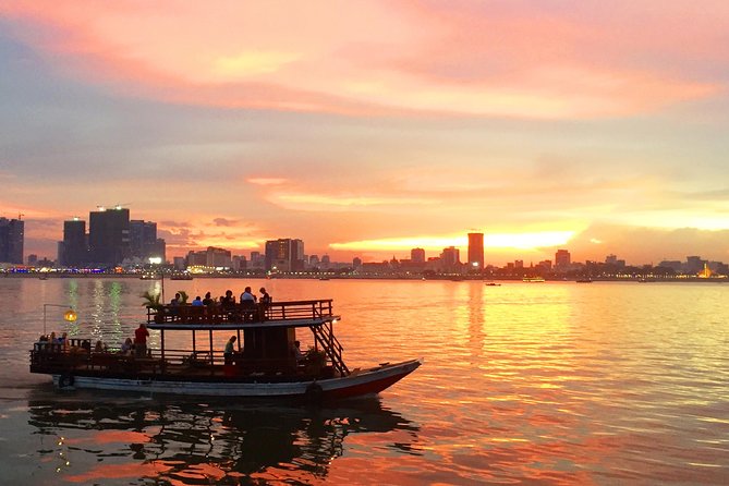A sunset view over the Mekong River in Phnom Penh, Cambodia, featuring a boat with people enjoying the scenery and the city skyline in the background.