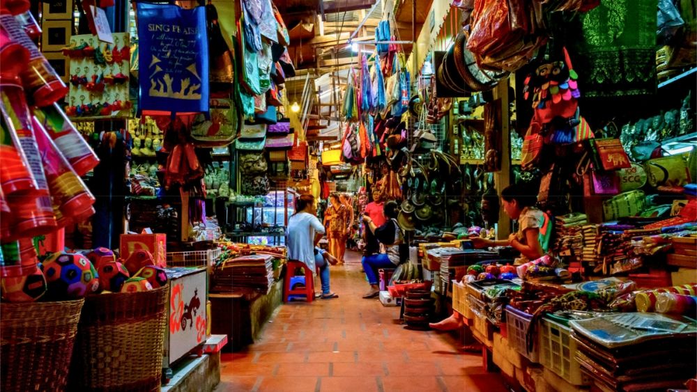 A bustling market in Phnom Penh featuring colorful stalls filled with handicrafts, souvenirs, and local goods, with shoppers navigating the vibrant atmosphere.