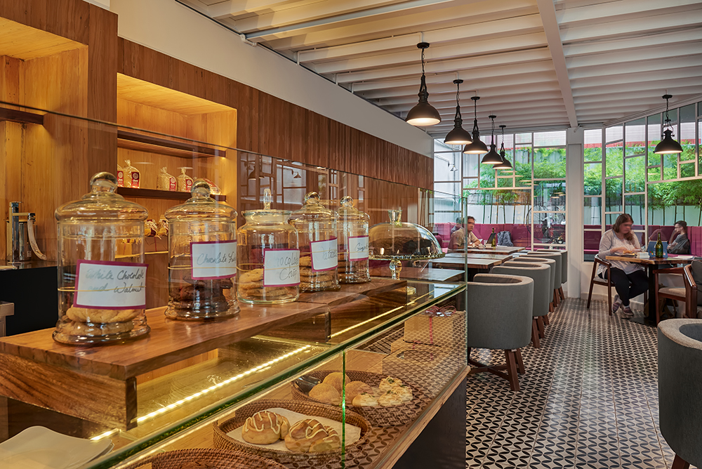 A modern cafรฉ interior featuring a display of glass jars filled with baked goods and a cozy seating area with patrons enjoying their meals.