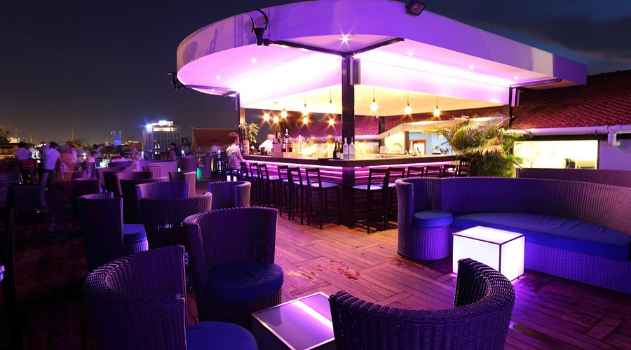 Rooftop bar with modern seating and vibrant purple lighting, showcasing a stylish atmosphere for enjoying drinks.