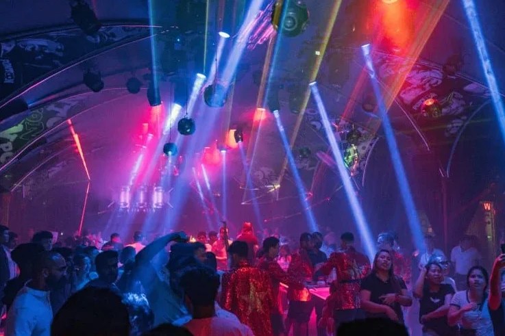 Crowd dancing on a vibrant dance floor in a club with colorful laser lights and an energetic atmosphere.