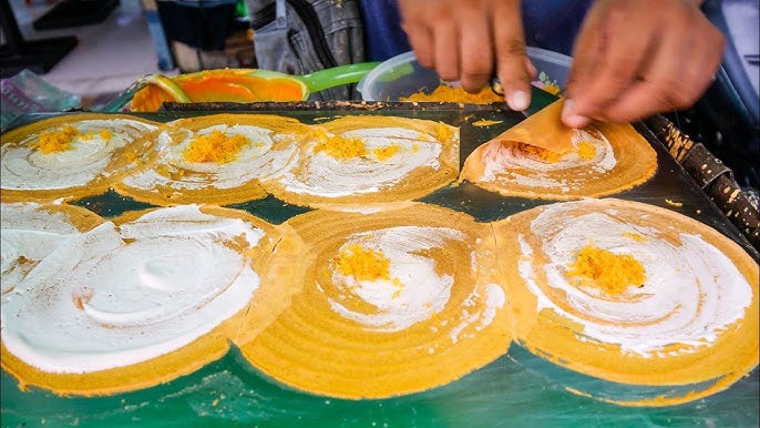A vendor preparing traditional Cambodian street food, with pancakes being filled with coconut and other ingredients on a griddle.