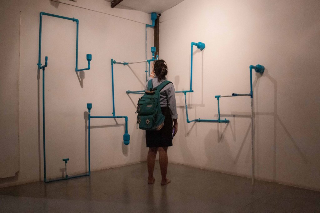 A visitor examining a minimalist art installation made of blue pipes on a white wall in a gallery.