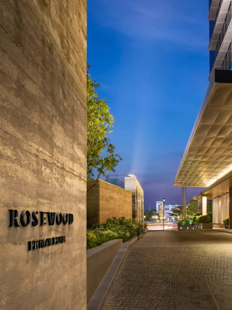 Exterior view of the Rosewood Hotel in Phnom Penh at dusk, showcasing modern architecture and a well-lit entrance.