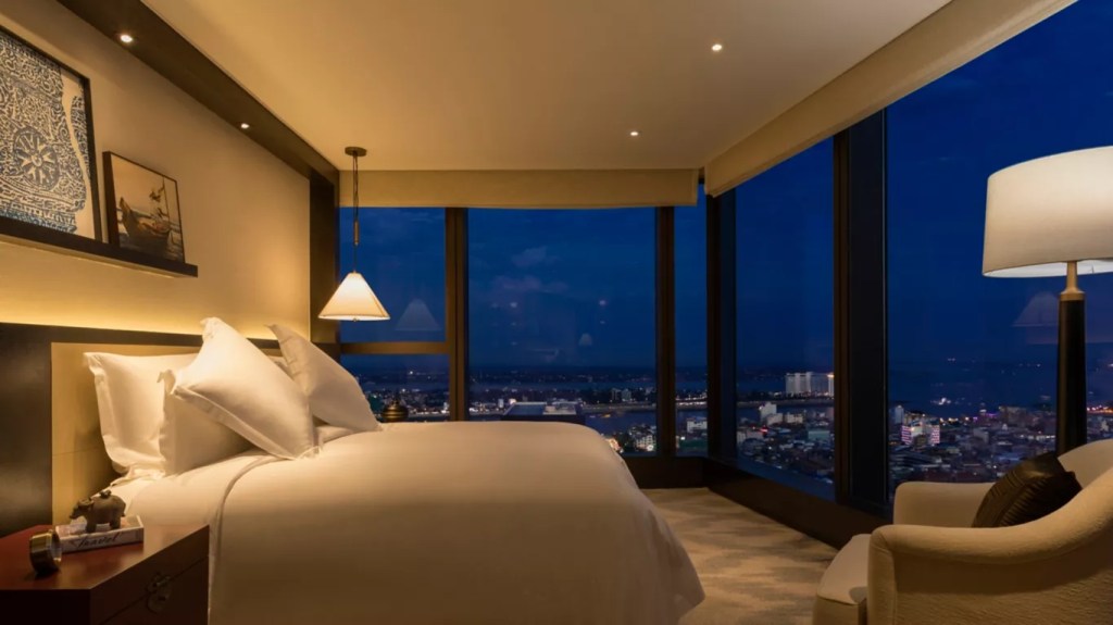 Luxurious hotel room at night with panoramic city views, featuring a plush bed and modern decor.