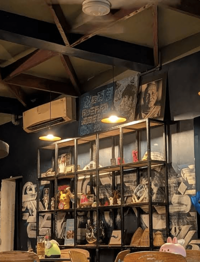 Interior of a cozy bar showing a wooden shelf display filled with unique decorations, art pieces, and a warm ambiance created by hanging lights.