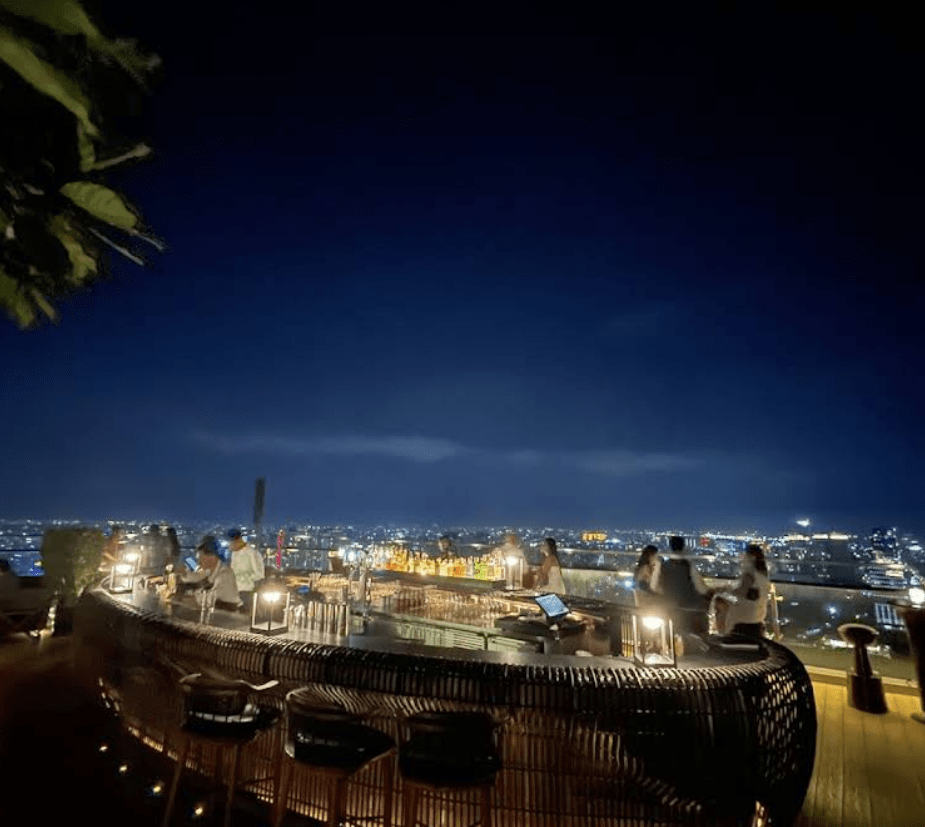 A luxurious rooftop bar in Phnom Penh overlooking the city skyline at night, with patrons enjoying drinks and a vibrant atmosphere.