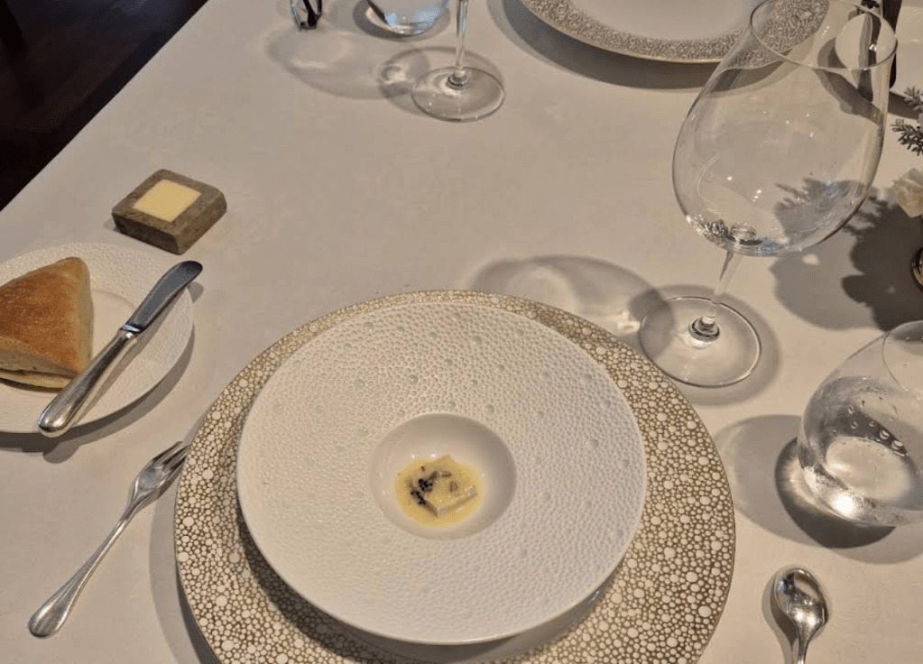 Elegant table setting featuring a fine dining dish with artistic plating, accompanied by a piece of bread and glassware.