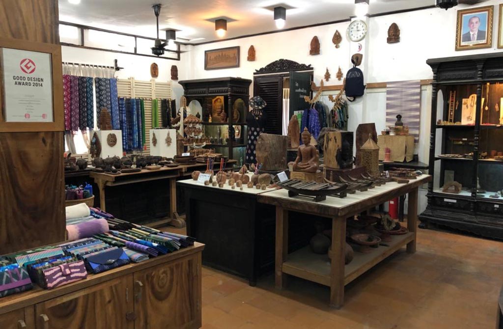 Interior view of a craft shop in Phnom Penh showcasing traditional textiles, wooden sculptures, and artisan crafts, with a warm ambiance and various colorful products displayed.