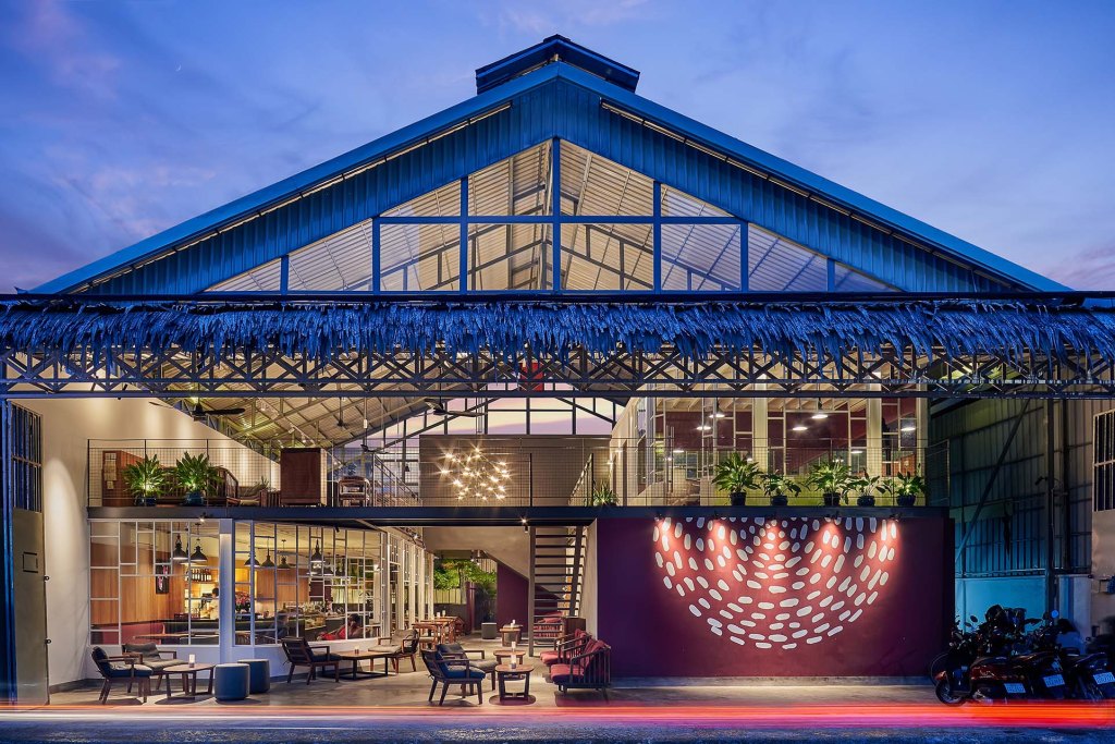Exterior view of a modern art space with a large glass roof and a colorful wall installation, showcasing a lively atmosphere in Phnom Penh.