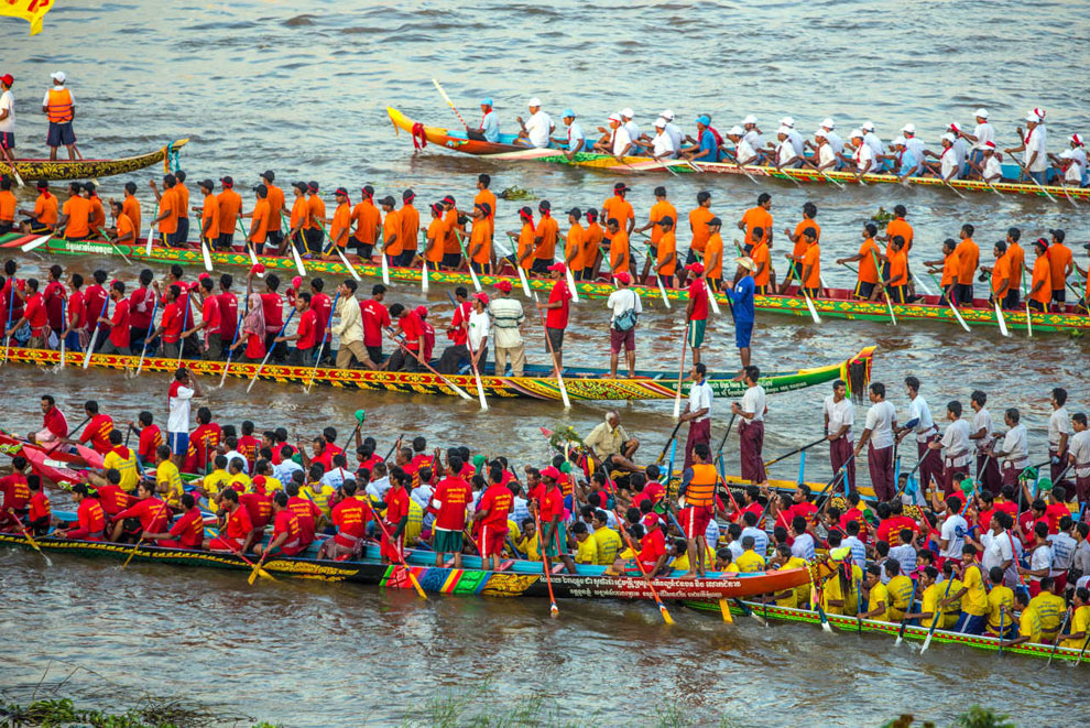 A vibrant boat race with teams in colorful uniforms paddling on the river, showcasing traditional Khmer culture during a festive event.