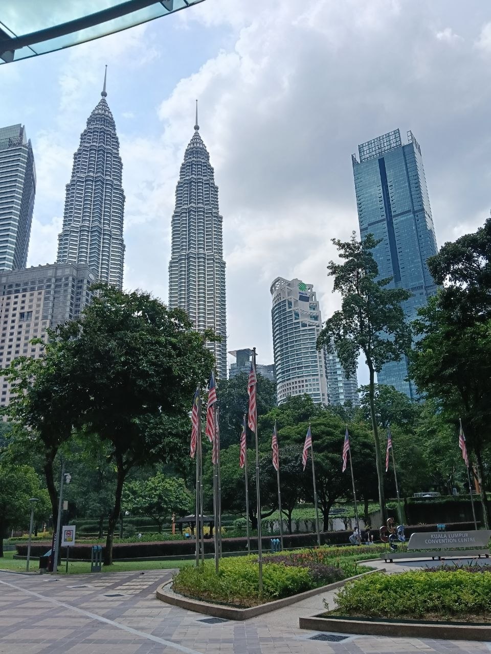 KLCC Park with Malaysian flags and the Petronas Twin Towers rising behind lush green trees