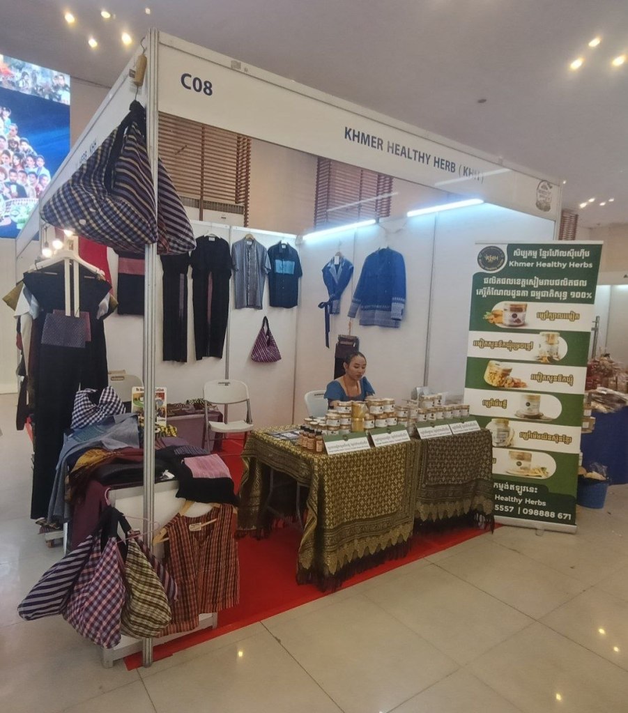  A vendor at the Khmer Healthy Herbs stall at the Khmer Food Must Be Strong exhibition, displaying traditional Khmer clothing and locally made herbal products at Koh Pich Theater 2026