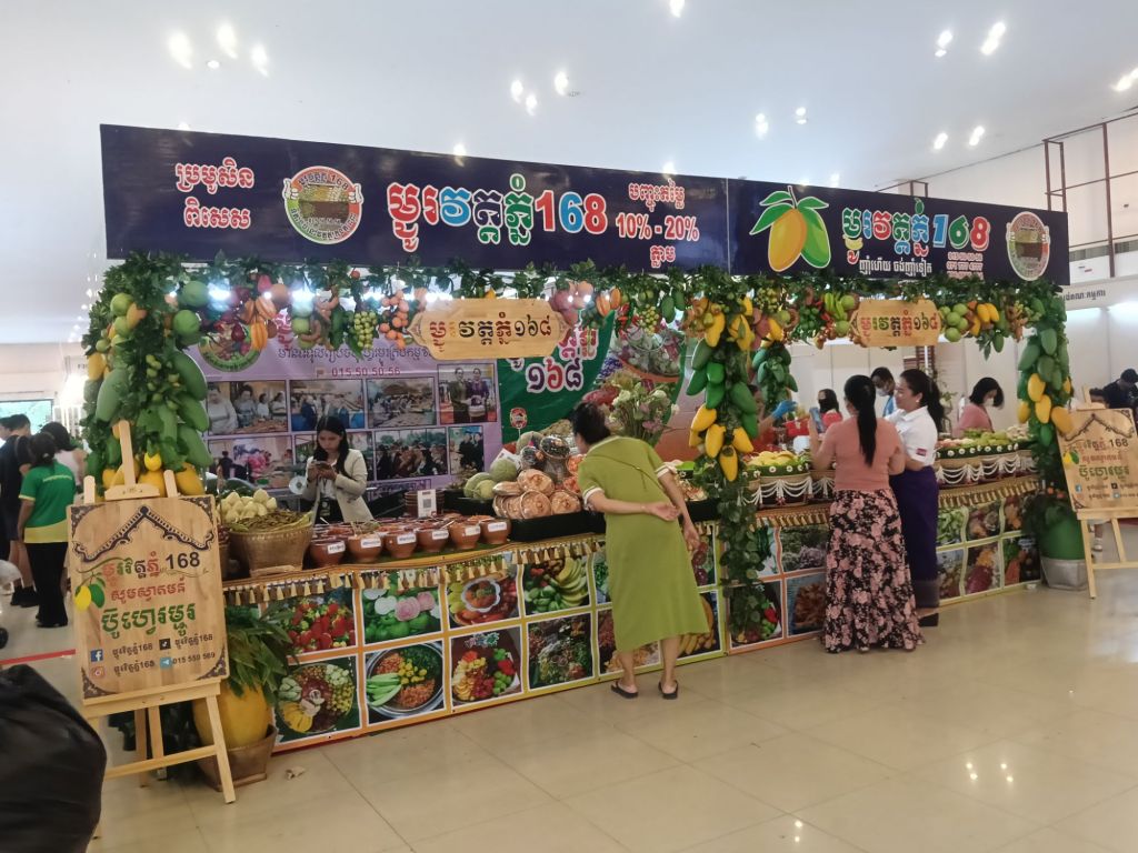 Visitors browsing the Phnom Penh 168 fruit and produce stall at the Khmer Food Must Be Strong exhibition, with a colourful display of tropical fruits, jams and preserved Cambodian food products at Koh Pich Theater 2026
